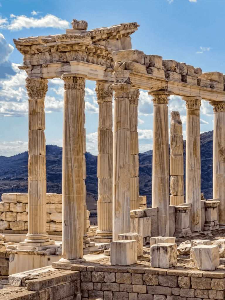 Ancient Greek ruins with tall Corinthian columns and marble architecture under a bright blue sky.