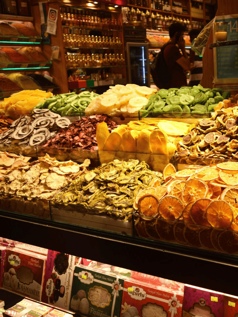 Dried fruit and snack displays at a market, with colorful packaging and a shopper in the background.