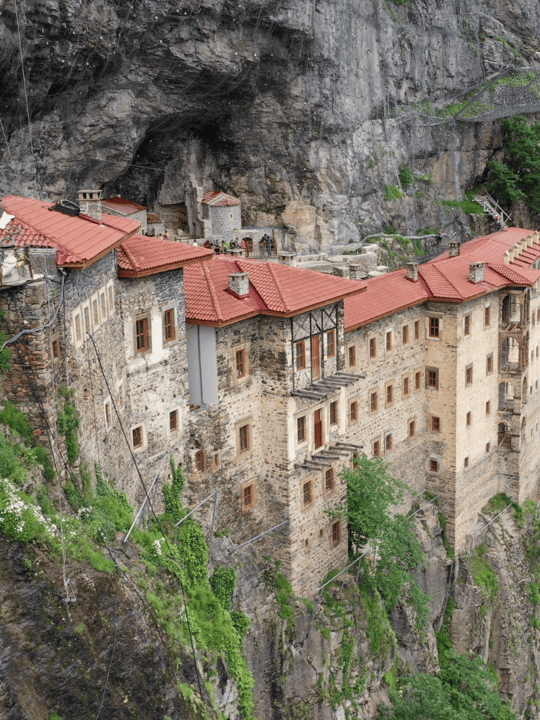 Ancient cliffside monastery with red-tiled roofs and stone walls nestled on a rocky precipice.