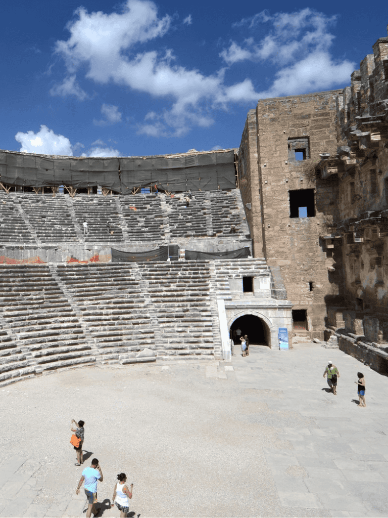 Ancient Roman amphitheater with stone seating and historic architecture under a bright blue sky.