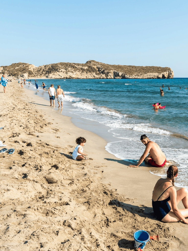 Kids playing on sandy beach with blue ocean and rocky cliffs in background.