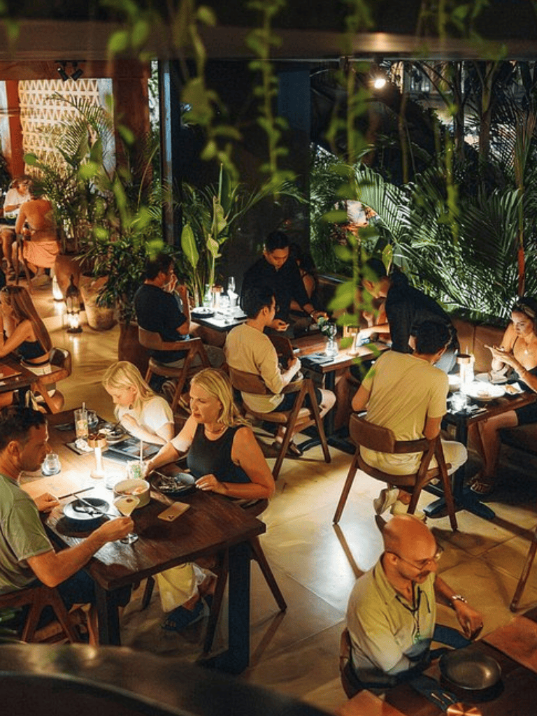 Relaxed indoor dining at a lush, botanical restaurant with diverse guests enjoying meals amidst greenery.