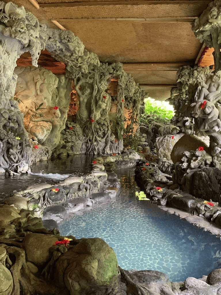 Intricate stone carvings of Hindu deities and nature scenes at a tranquil outdoor water temple.