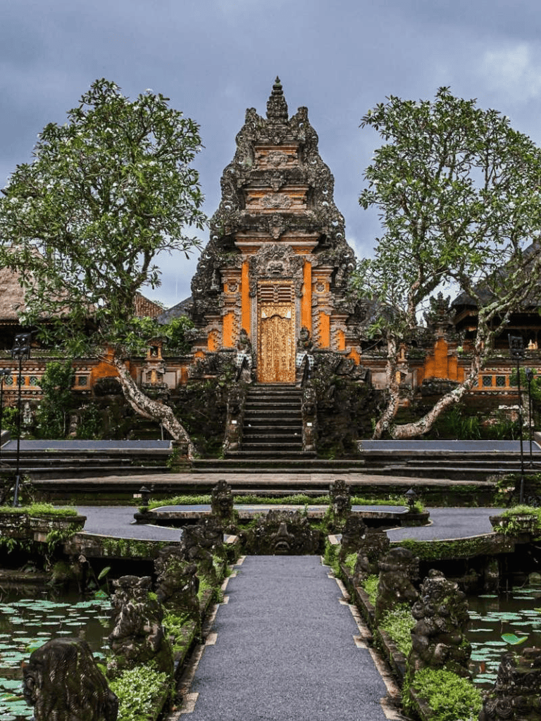 Ancient Balinese temple with lush gardens and water features, surrounded by traditional architecture.