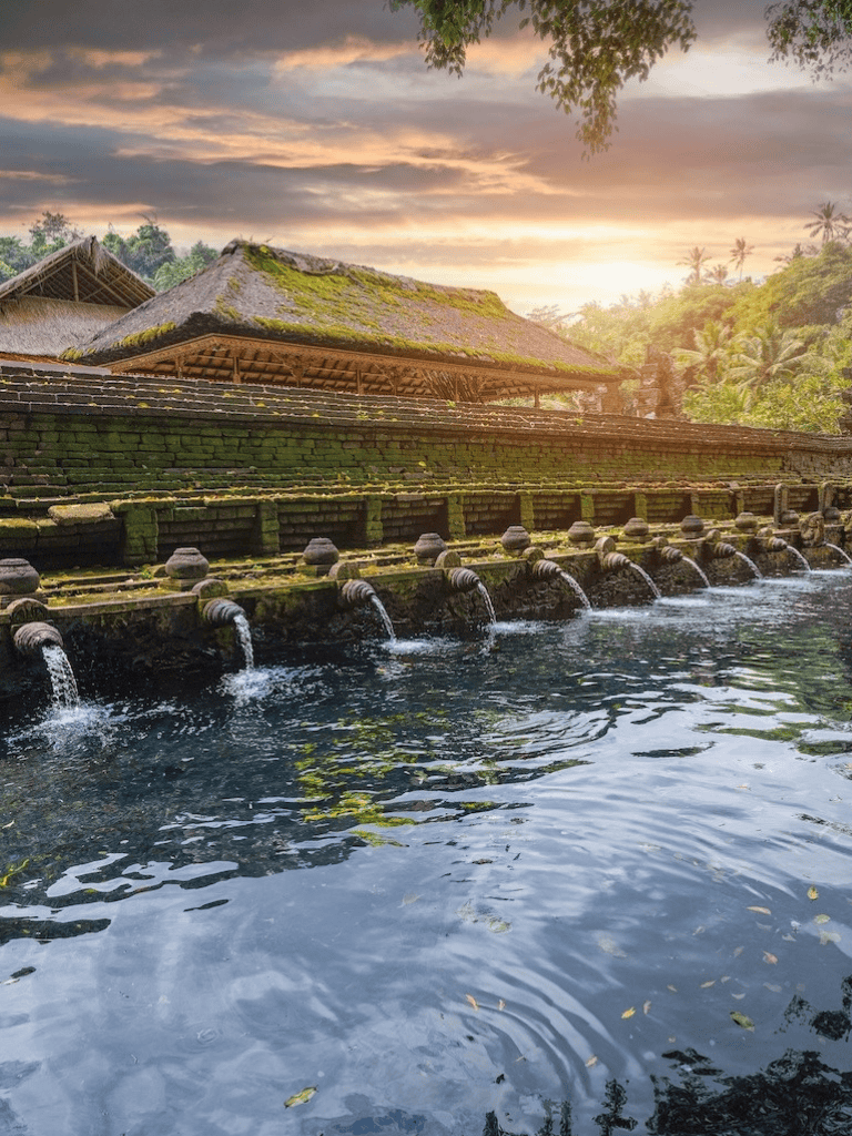 Ancient water temple with cascading water in lush jungle at sunset.