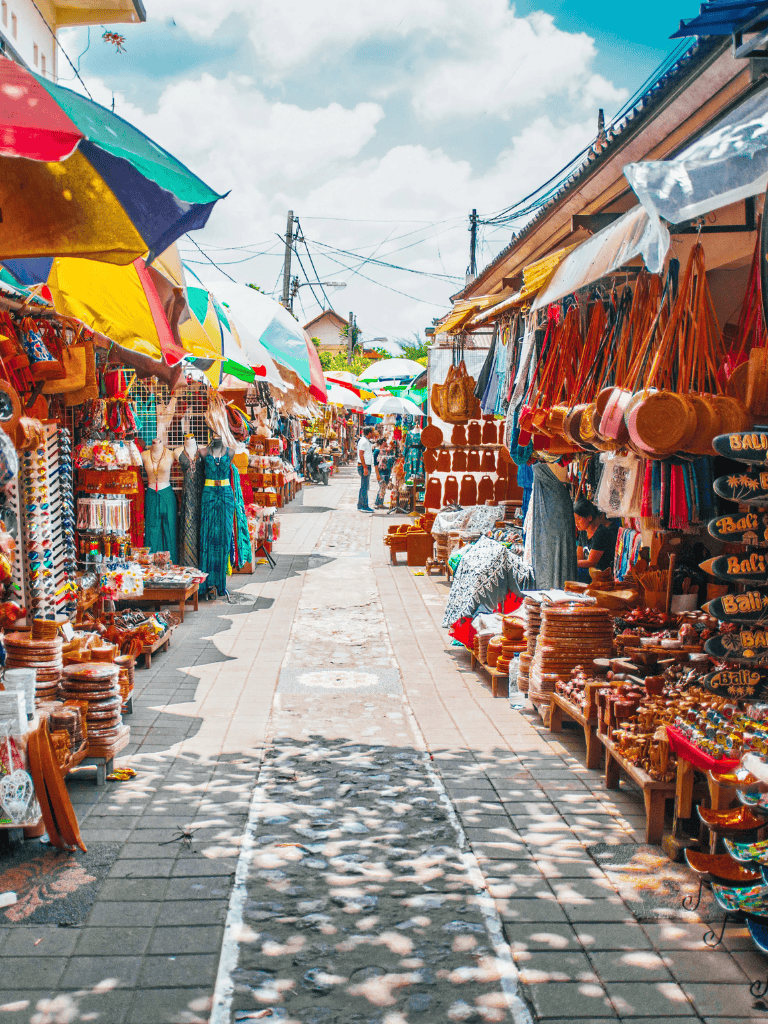 Colorful outdoor market stall with handmade crafts and souvenirs under umbrellas on a sunny day.
