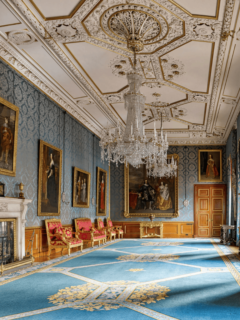 Luxurious royal salon with grand chandelier, ornate ceiling, classic portraits, and elegant furnishings.