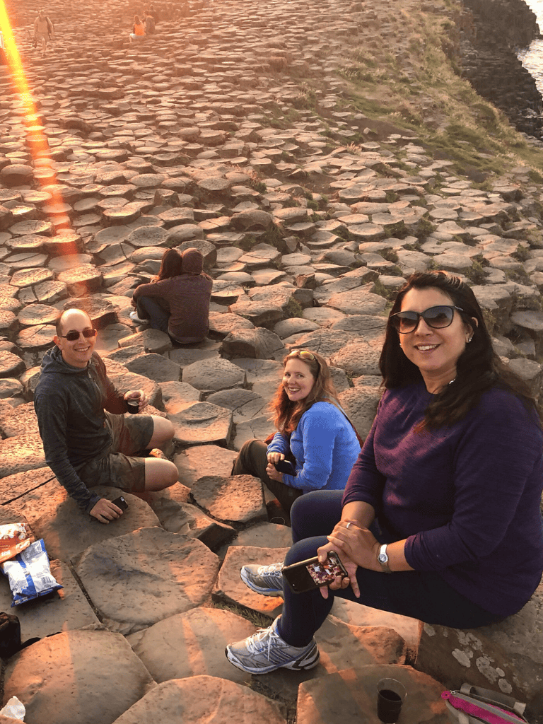 Scenic coastal walk with friends on Giant's Causeway basalt stepping stones, sunset view.