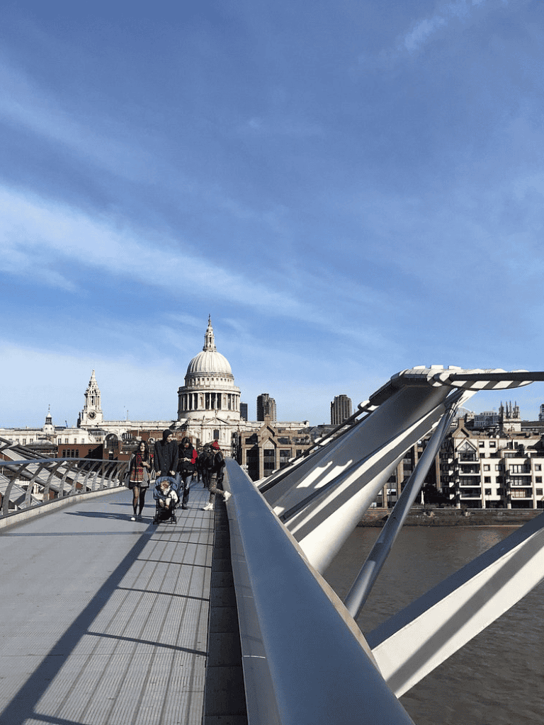 Modern London Millennium Bridge with St. Paul's Cathedral in the background, scenic cityscape, and pedestrians walking.