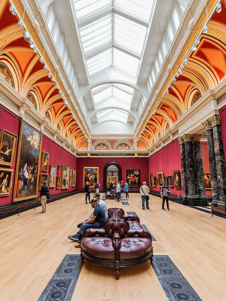 Ancient art museum interior with classical paintings, ornate architecture, and visitors exploring artwork.