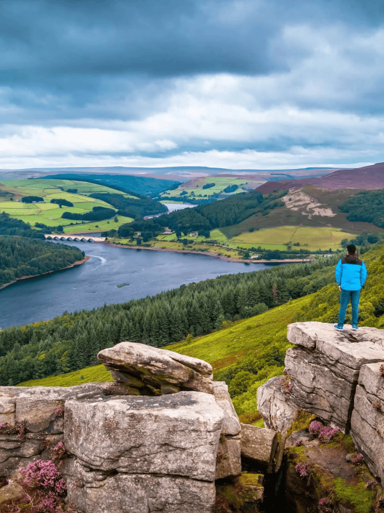 Breathtaking landscape with river, rolling hills, and a hiker on rocky viewpoint.