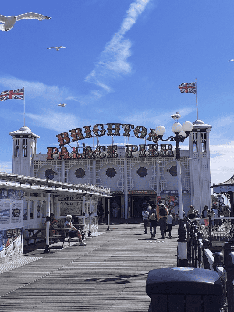 Seaside Brighton Palace Pier with tourists and seagulls under blue sky, iconic British landmark, seaside entertainment.