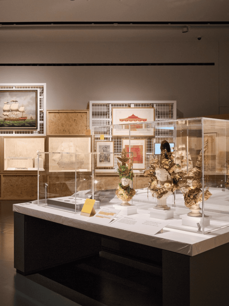 Intricate antique porcelain vases displayed in museum exhibit with framed artwork in background.