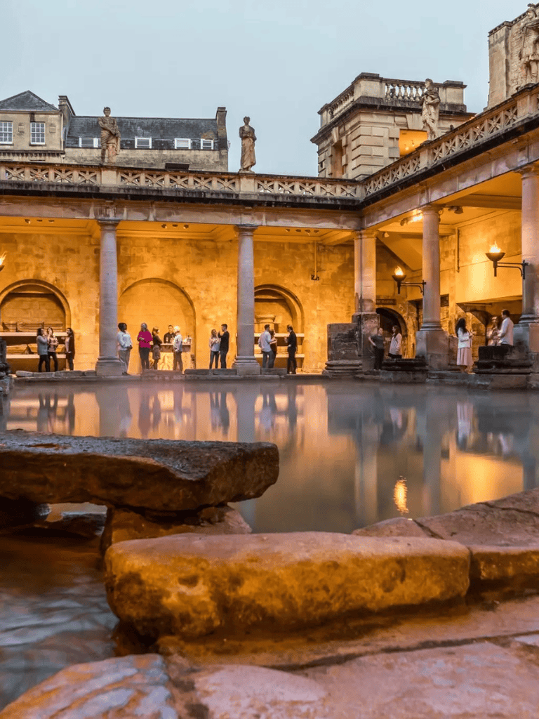 Ancient roman-style bathhouse with columns and people relaxing, historical architecture, beautiful evening ambiance.