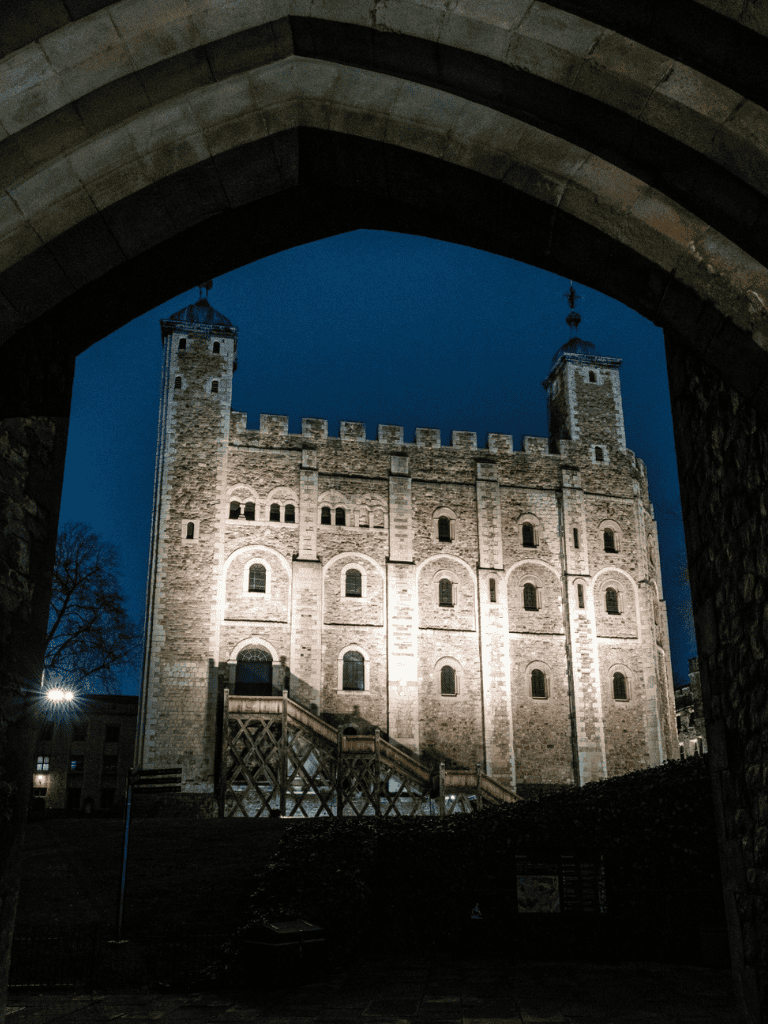 Stone castle illuminated at night through an archway, highlighting medieval architecture and historic charm.