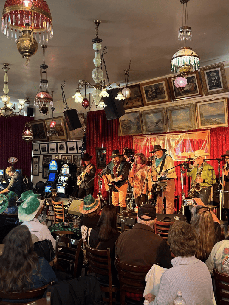 Live country band performance at a cozy, vintage-themed venue with framed artwork and elegant chandeliers.