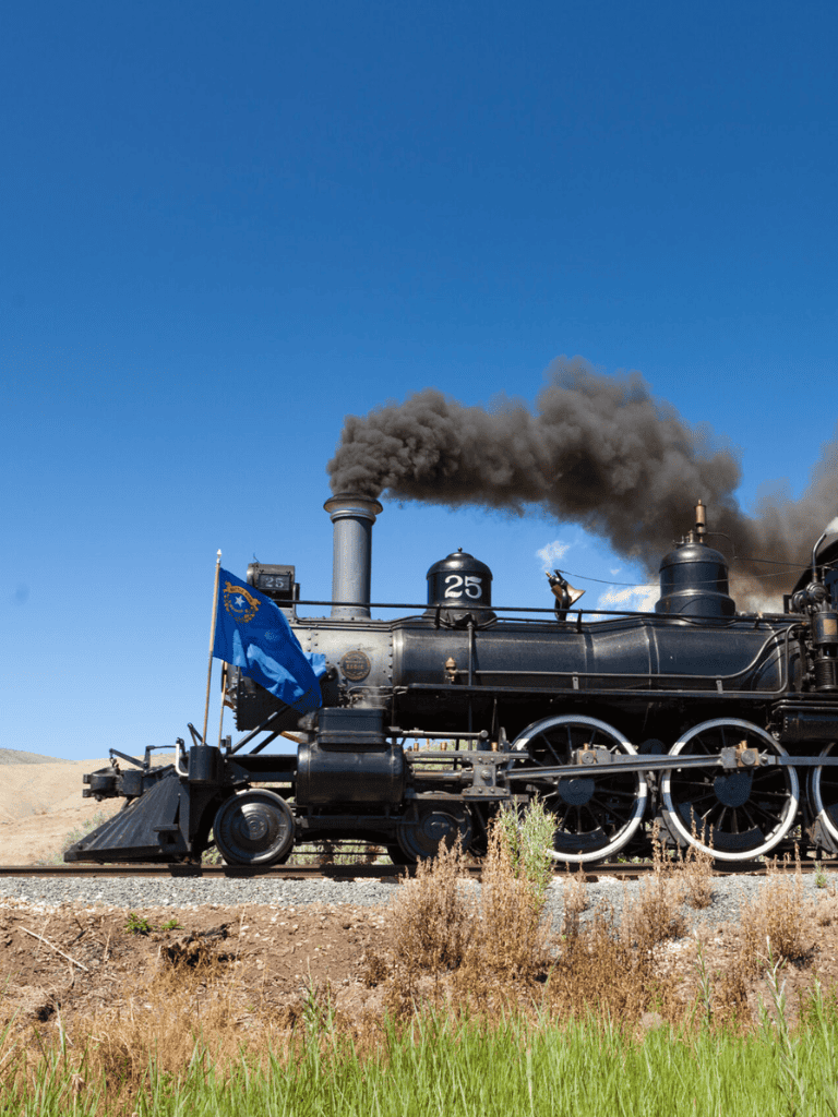 Smoke-emitting vintage steam locomotive on tracks in a rural setting, blue sky.