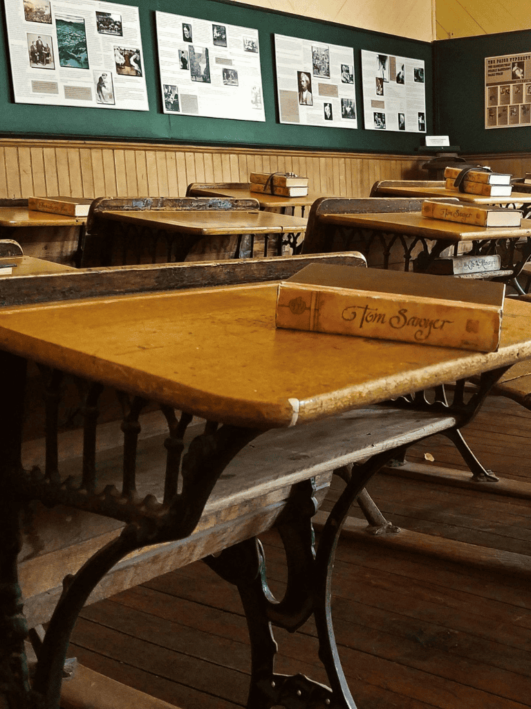 Inkwell school desk with old books on wooden classroom table, historical education setting.