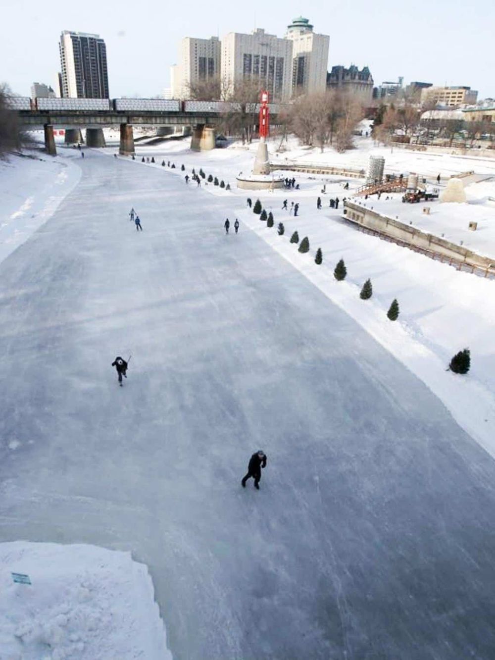 Smooth ice skating rink in downtown with city skyline and snow-covered surroundings.