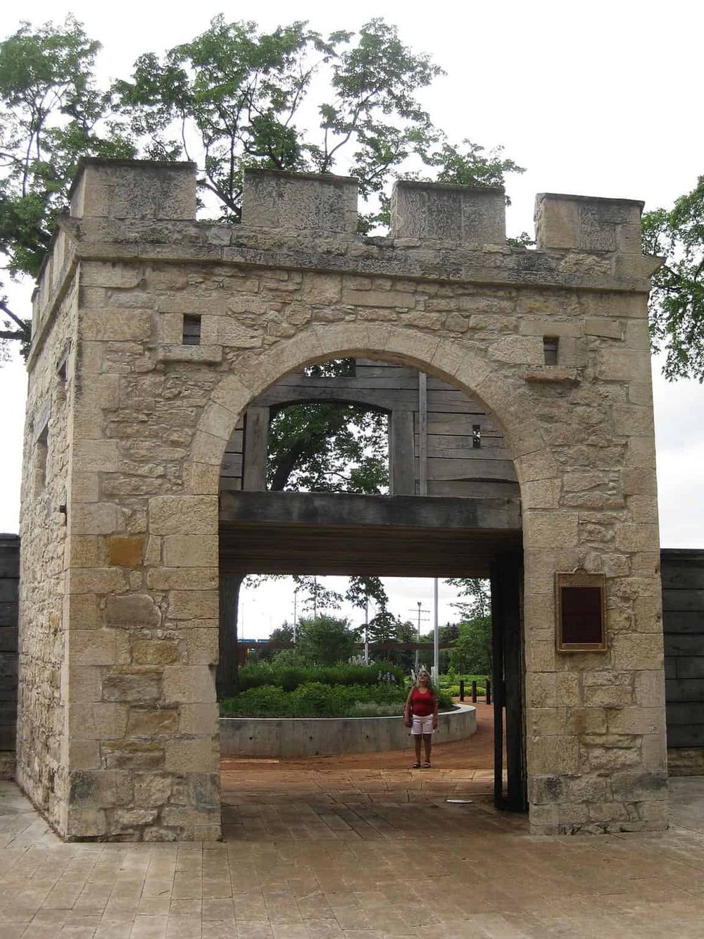 Ancient stone archway with a person standing beneath, surrounded by greenery, showcasing historical architecture and travel destinations.