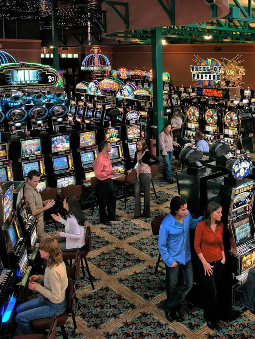Brightly lit casino with numerous slot machines, colorful lights, and visitors enjoying gambling activities.