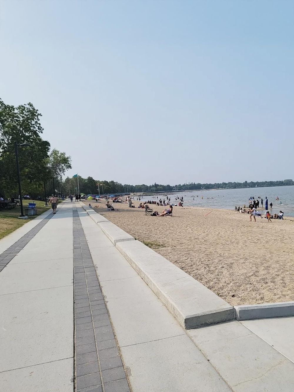 Scenic lakeside walk with people relaxing on the beach and enjoying water activities.