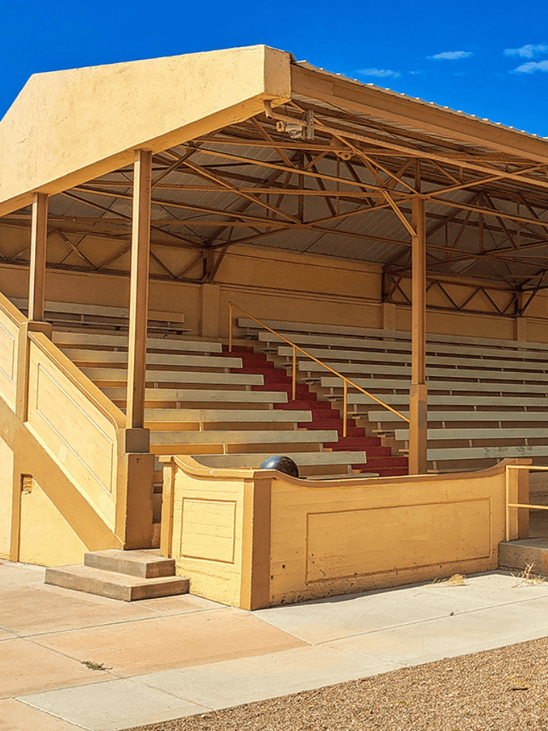 Stadium bleachers with yellow railings and a shade cover under a blue sky.