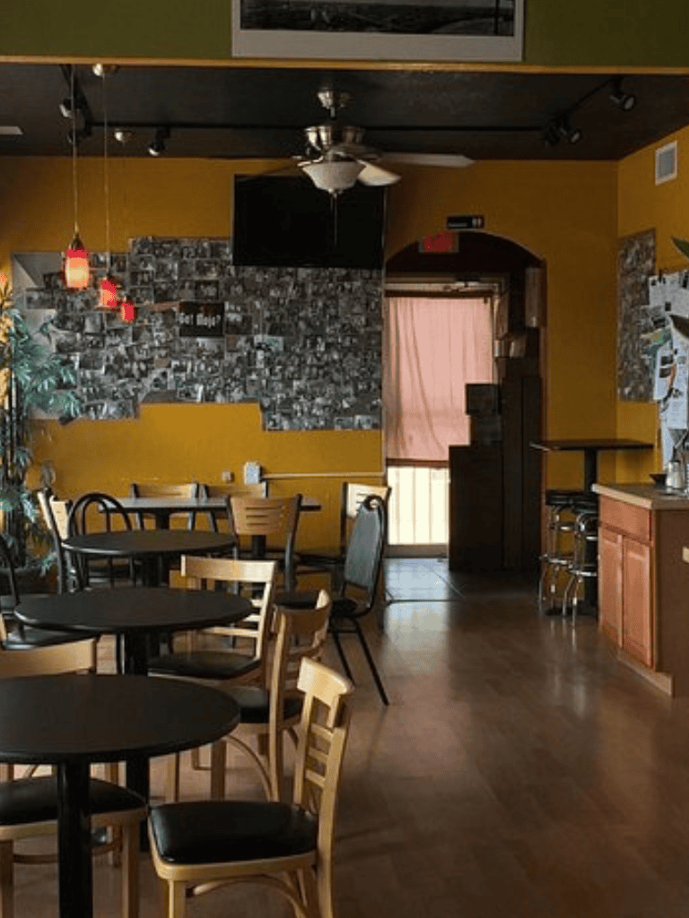 Cozy cafe interior with warm yellow walls, black tables, and a collage wall of photos, perfect for relaxing and dining.