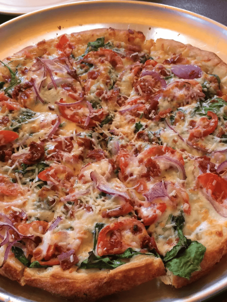 Cheddar, tomato, bacon, and spinach pizza on a golden crust. Perfect for different tastes, freshly baked at QuestForDirections.