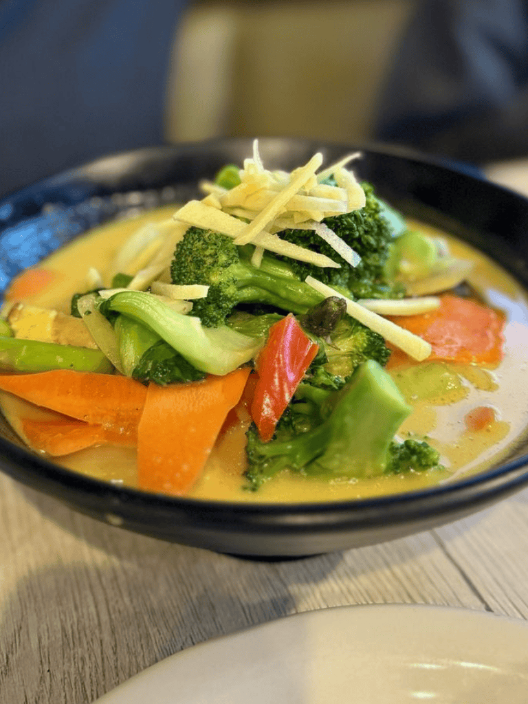 Steamed vegetable curry in a black bowl showing fresh broccoli, carrots, and peppers.