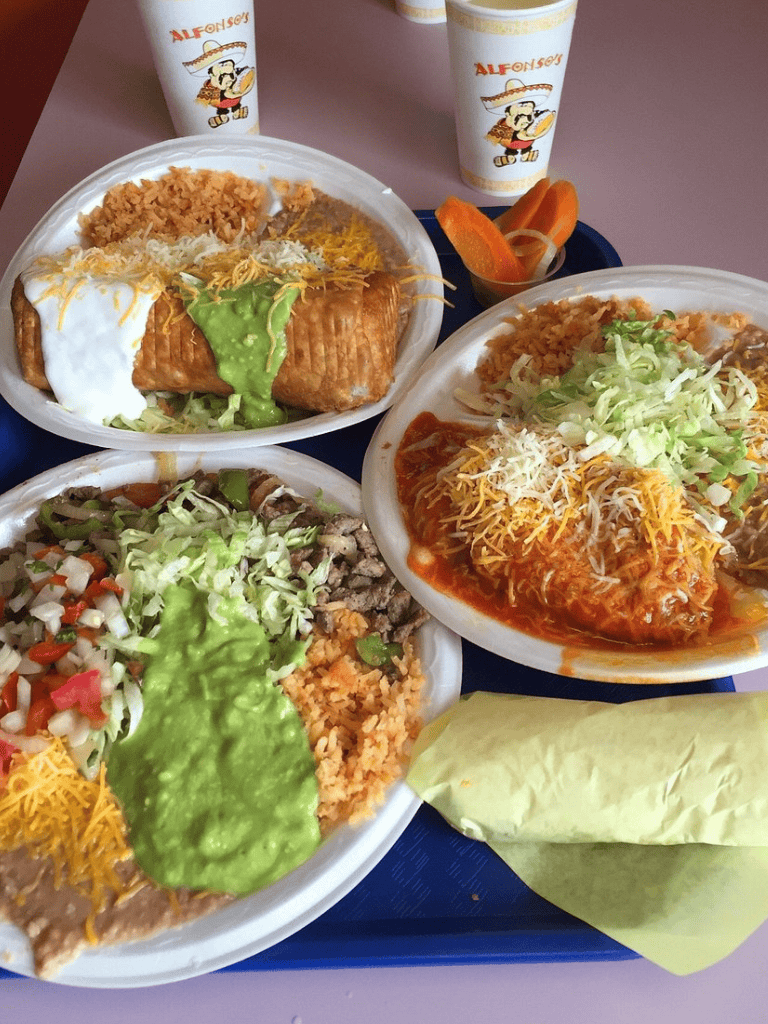 Cheesed enchiladas with rice, beans, and salsa, served with drinks at Quest for Directions Mexican restaurant.