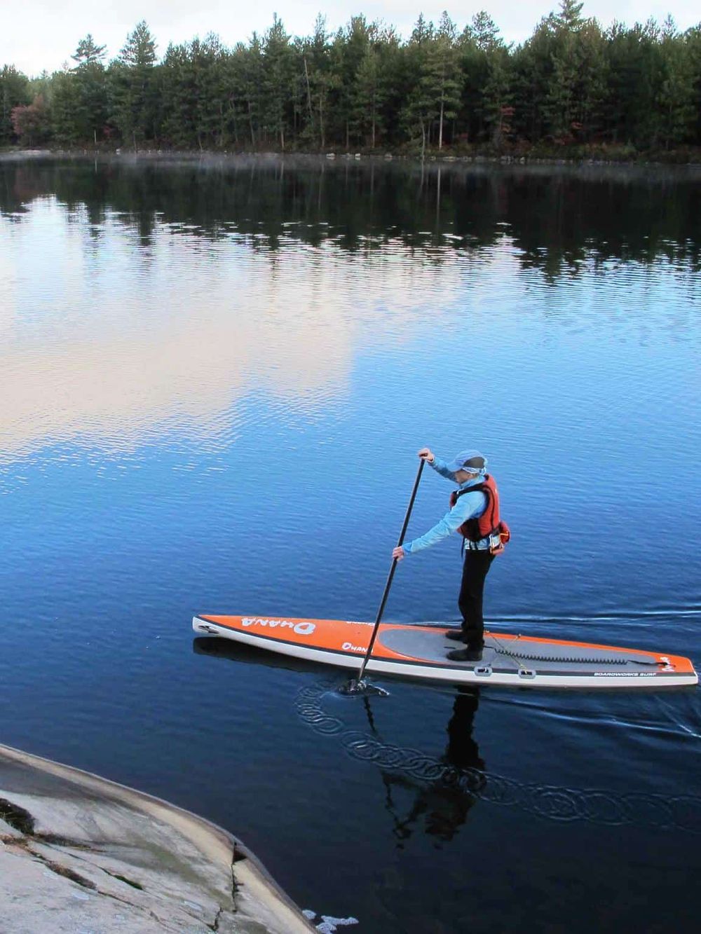 Serene paddleboarding on a calm lake surrounded by lush trees, perfect for outdoor adventure and nature exploration.