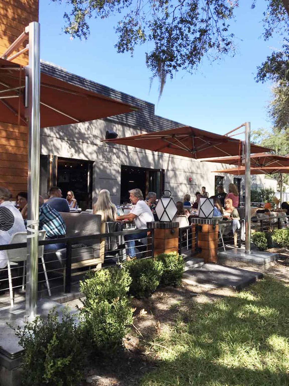 Outdoor dining patio at Quest for Directions restaurant with people enjoying meals under shade umbrellas.