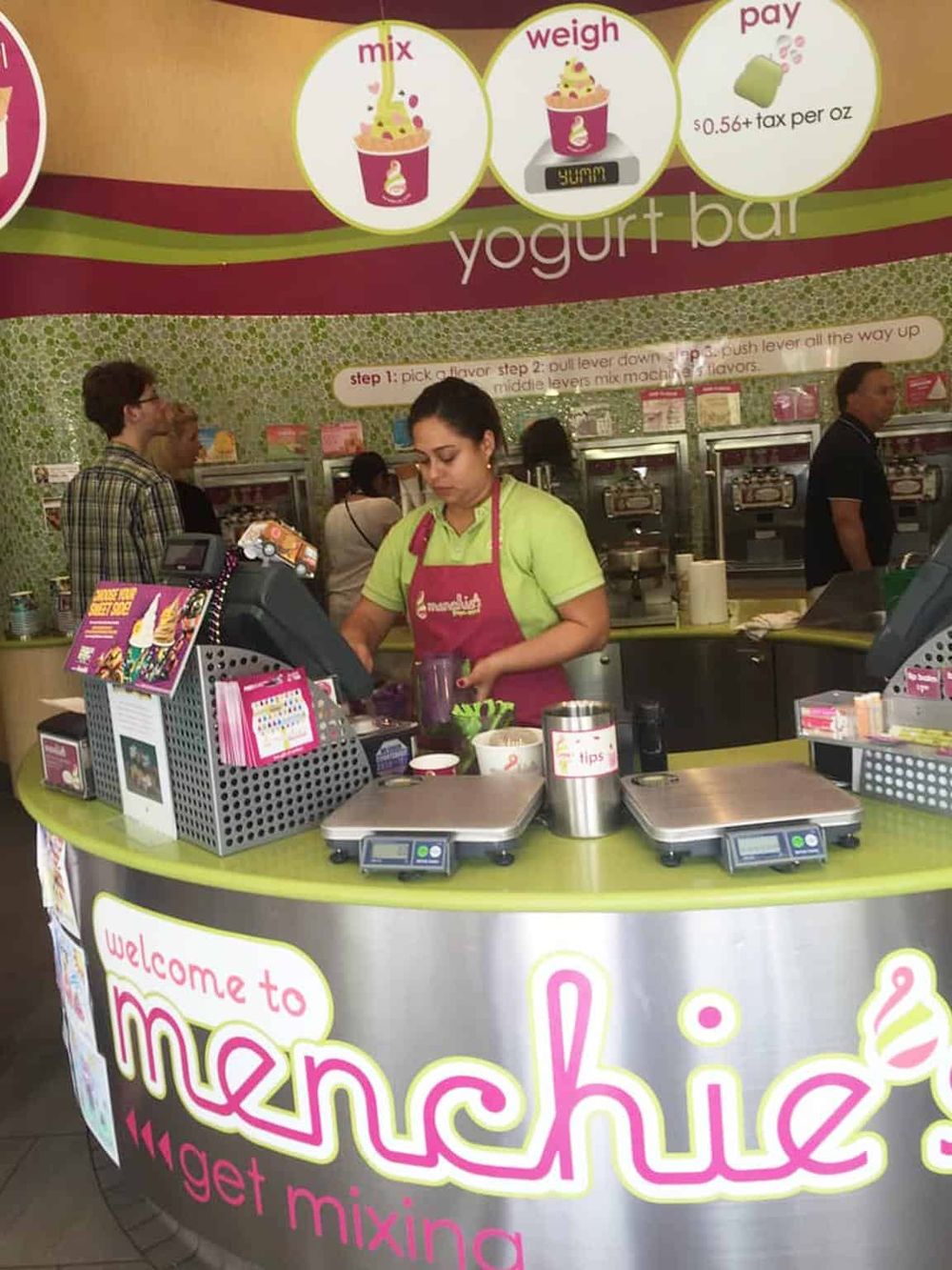 Fresh yogurt bar counter at Menchie's, with staff preparing frozen yogurt in a vibrant store environment.
