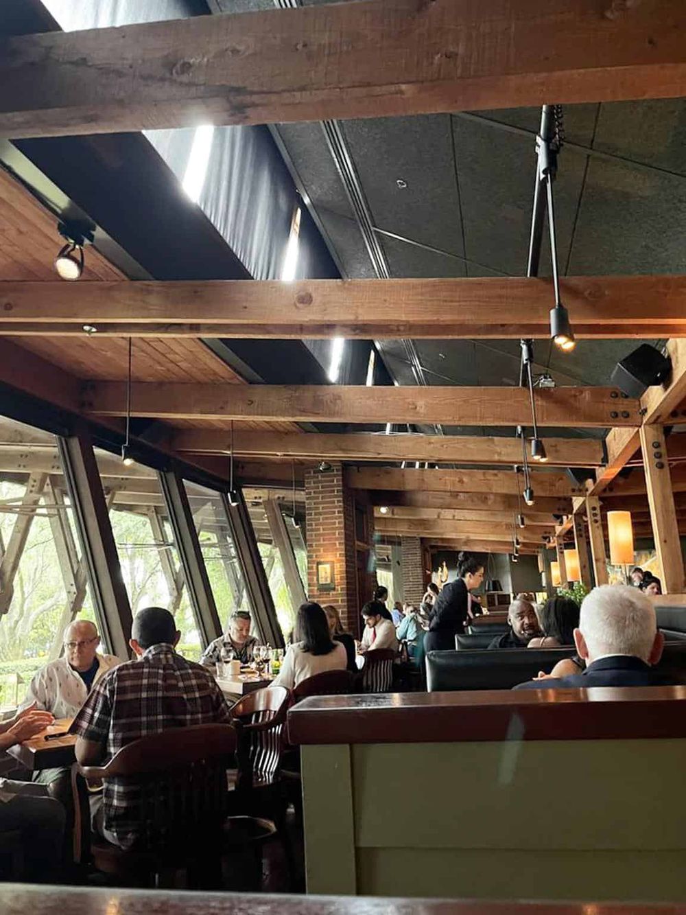 Cozy modern restaurant interior with wood accents, large windows, and diverse diners enjoying meals.