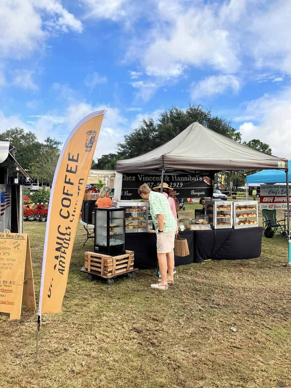 Freshly baked pastries at outdoor food vendor stand in park with colorful signage and clear sky.