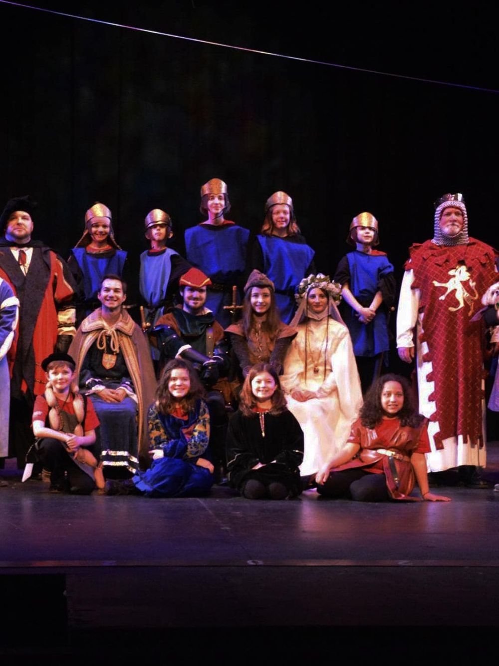 Children in medieval costumes performing on stage for a theatrical play.
