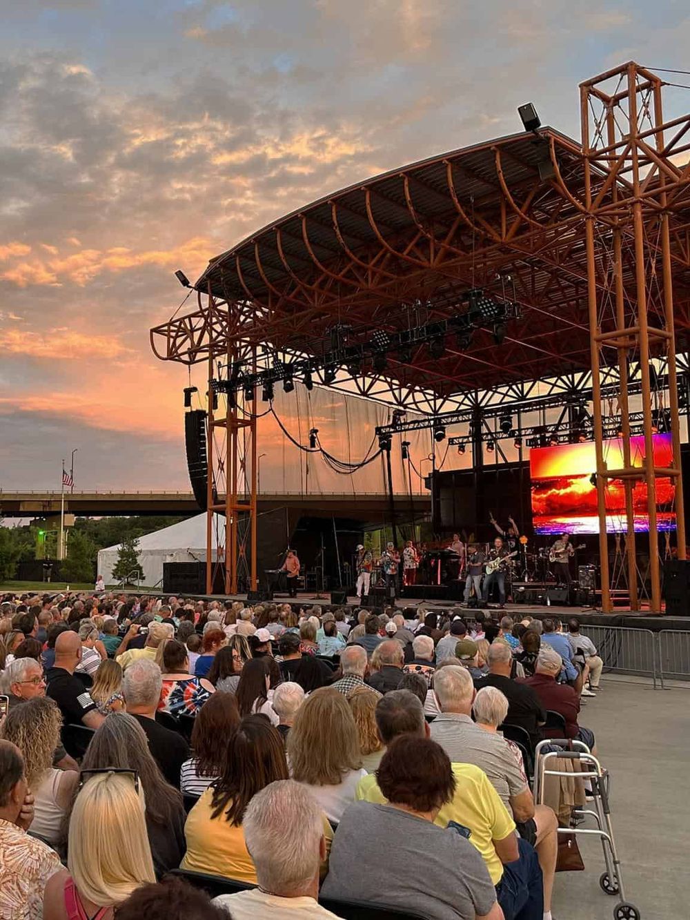 Open-air concert stage at sunset with a large crowd enjoying live music.