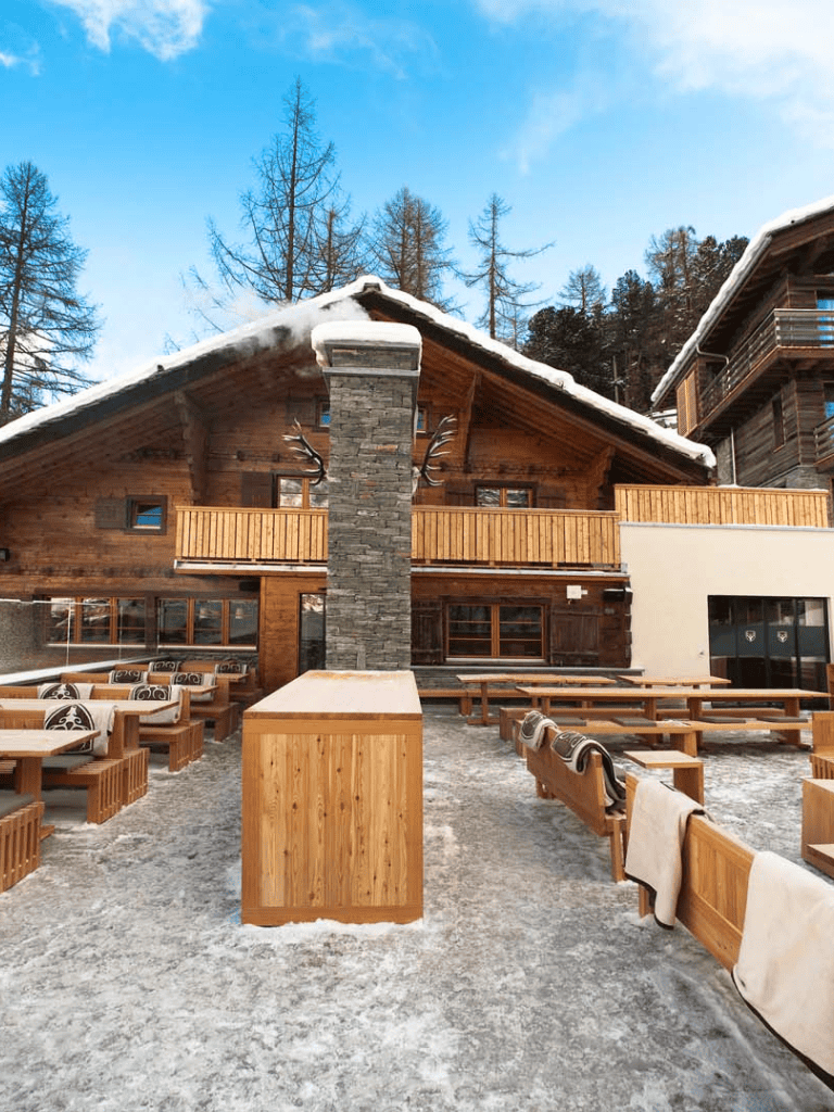 Cozy mountain chalet with outdoor seating and snow-covered terrace in a scenic winter setting.