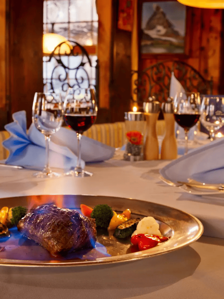 Juicy steak with vegetables on elegant restaurant table with wine glasses and candles.