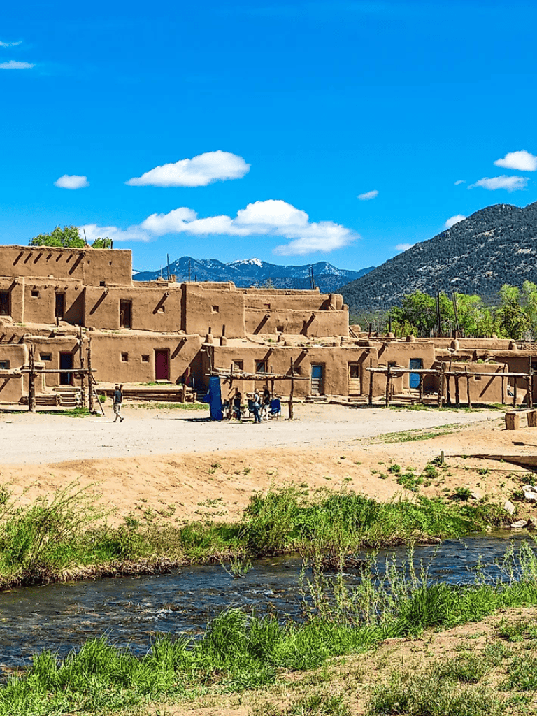 Traditional adobe houses in a scenic mountain landscape with a river in foreground.