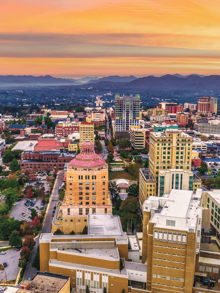 Vibrant cityscape of downtown with high-rise buildings and scenic mountain sunset in the background.