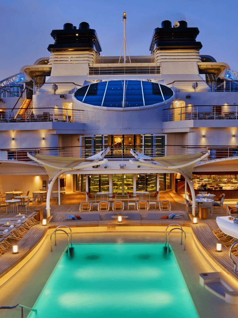 Luxurious cruise ship with pool and entertainment deck at dusk, offering a premium travel experience.