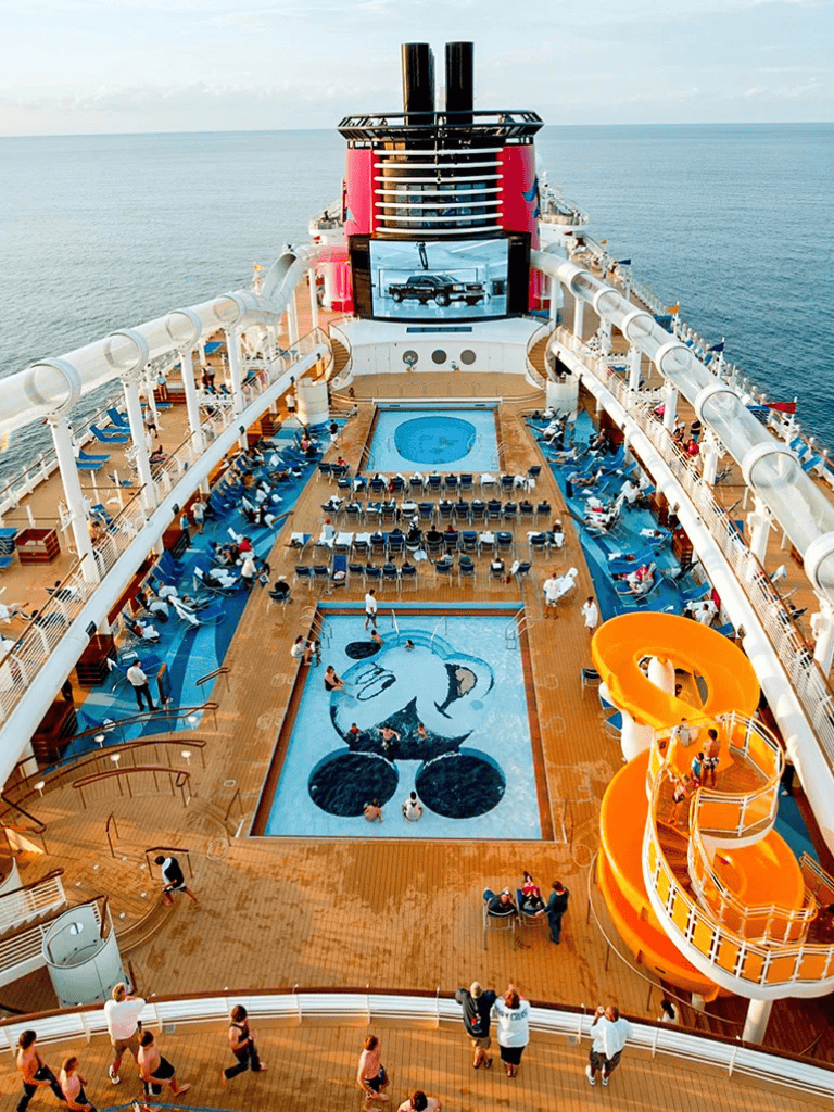 Aerial view of cruise ship pool area with water slide and ocean backdrop.