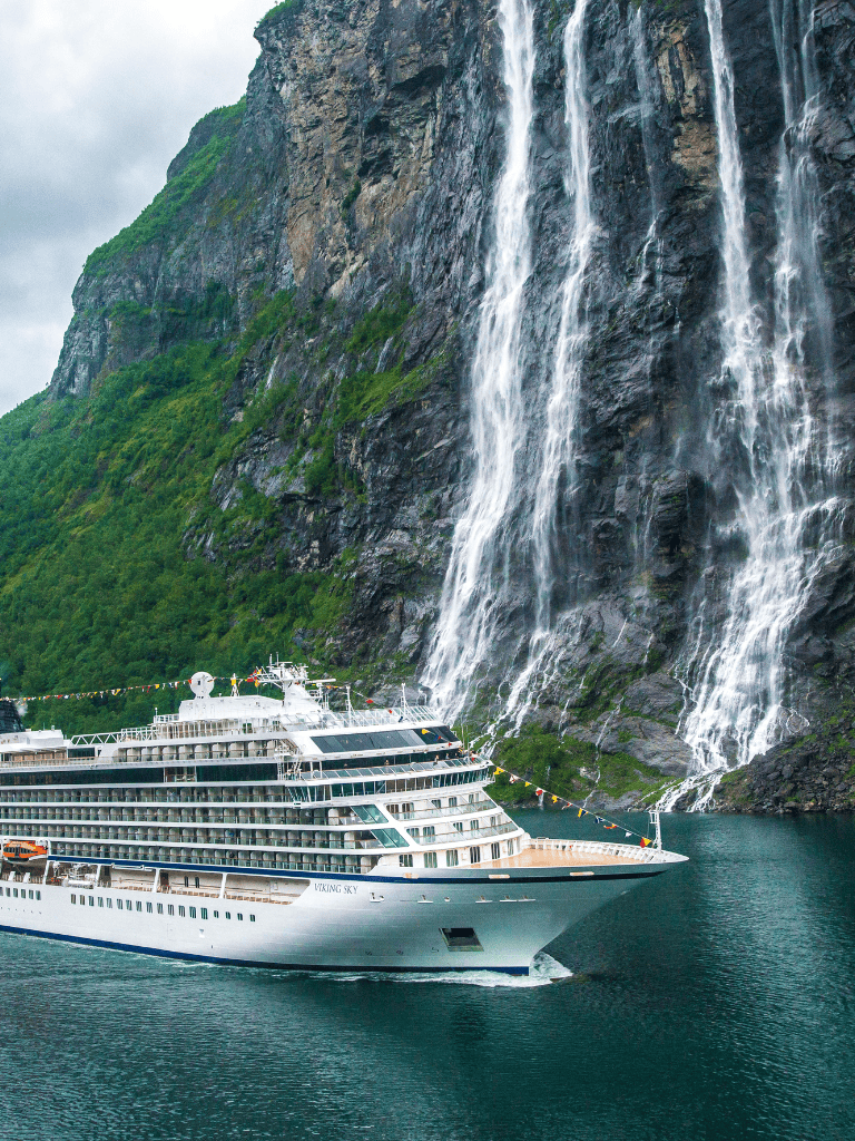 Luxurious cruise ship sailing past a stunning waterfall in fjord scenery.
