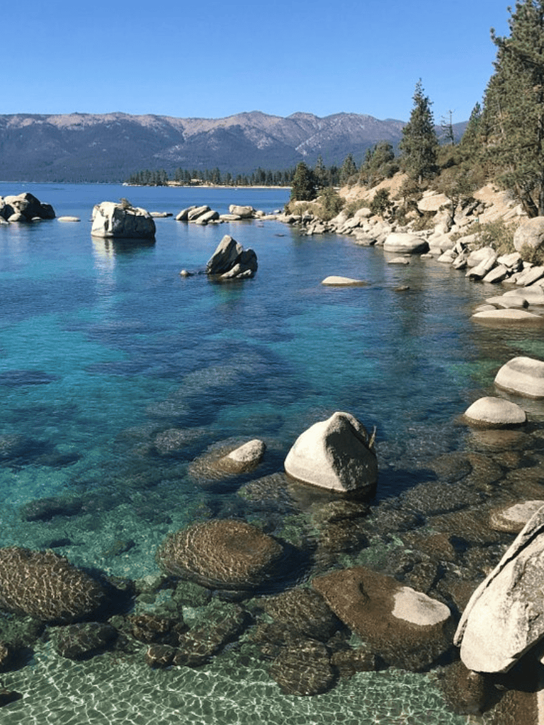 Serene lake with clear blue water, rocky shoreline, and distant mountains, perfect for outdoor adventures and nature exploration.