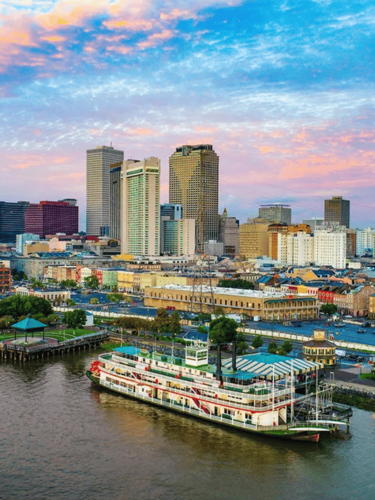 Downtown skyline with river cruise boat in New Orleans cityscape at sunset, vibrant city view.