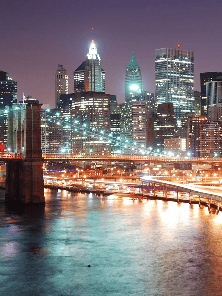 Bright New York City skyline with illuminated skyscrapers and Brooklyn Bridge at night.