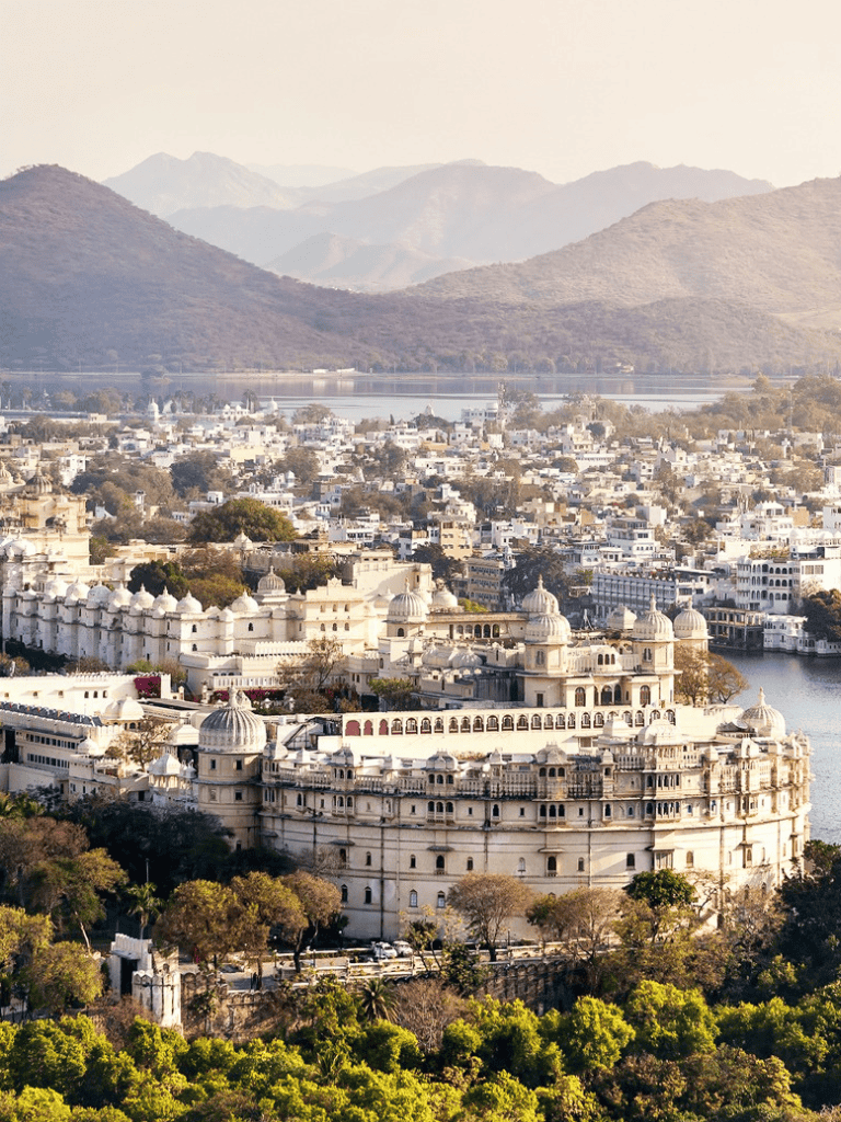 Majestic white palace overlooking city with mountains in background, scenic riverside view.
