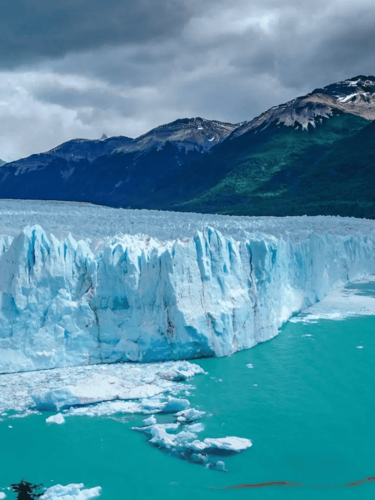 Vast glacier in icy blue waters with alpine mountains in the background, stunning natural landscape.
